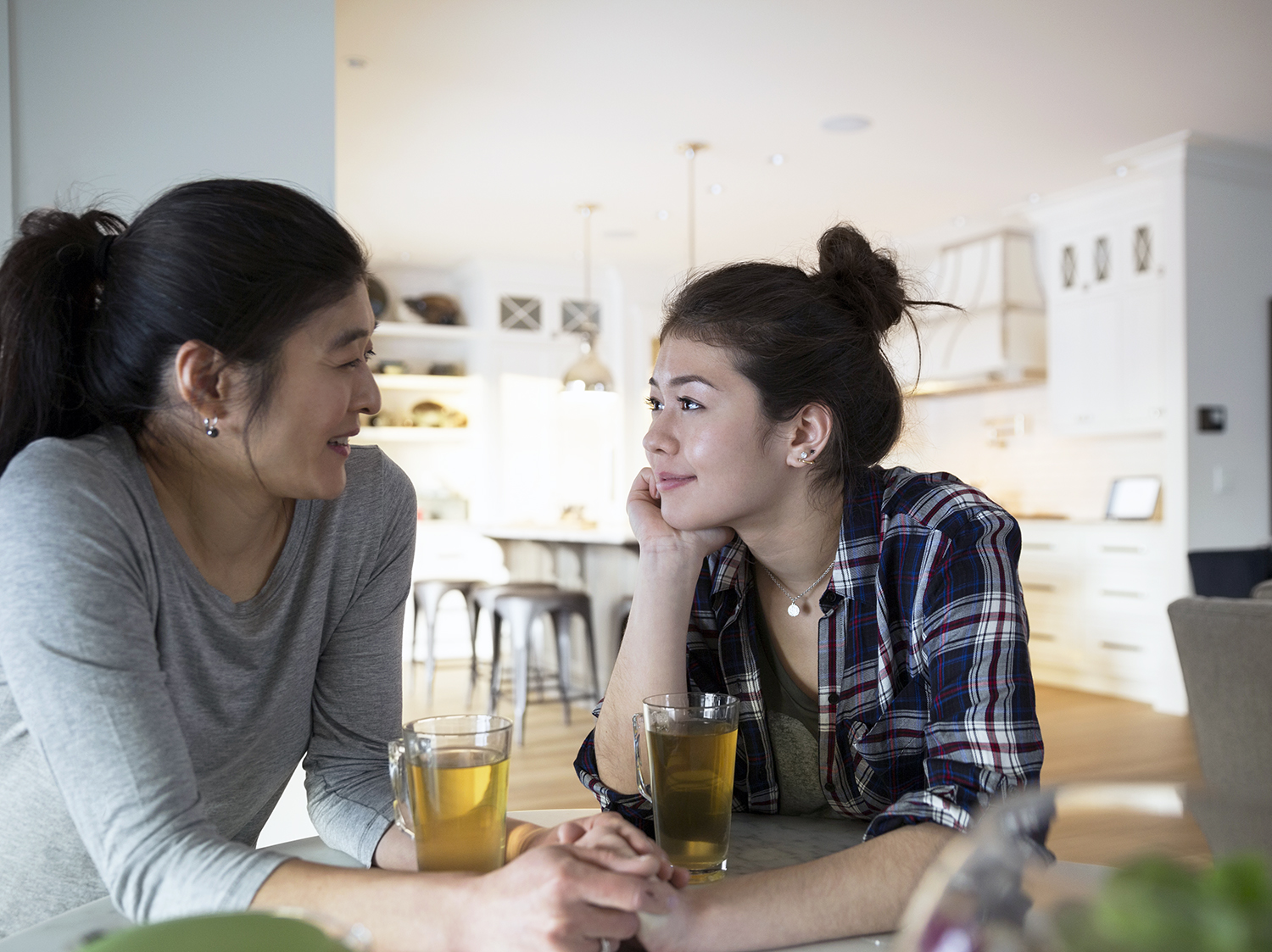 Mother and teenage daughter holding hands drinking tea