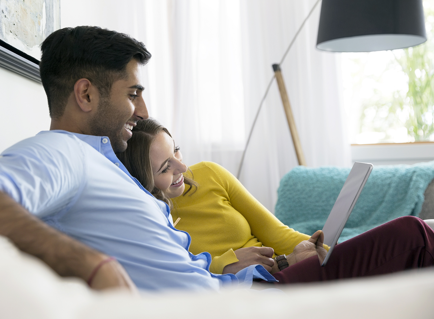 Young couple relaxing using digital tablet on living room sofa