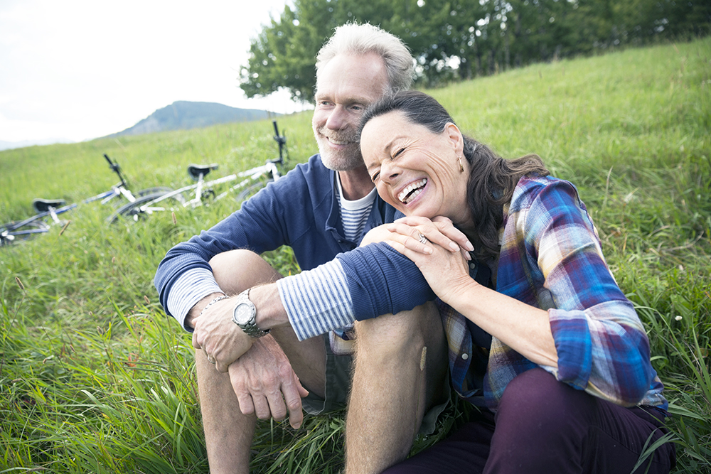 Laughing senior couple relaxing near mountain bikes in remote rural field