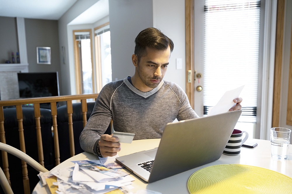 A man with credit card paying bills at laptop