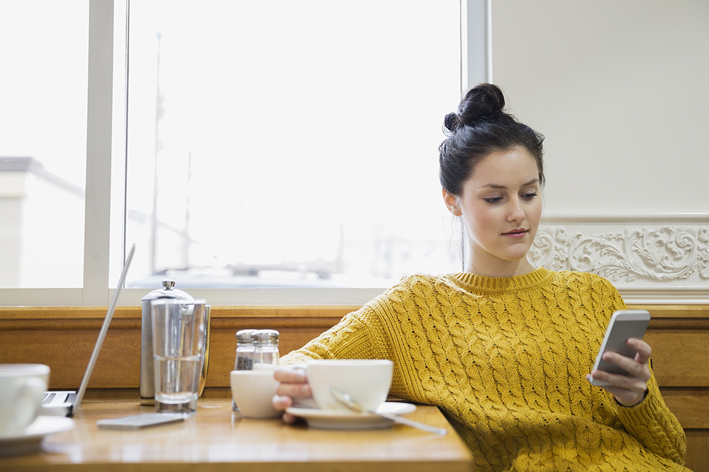 女人在咖啡館邊喝卡布奇諾，邊發短信