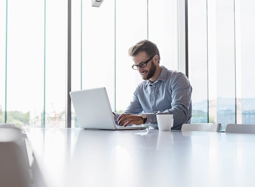 Man using laptop sitting at conference table in office