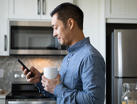 Man drinking coffee and using smart phone in morning kitchen