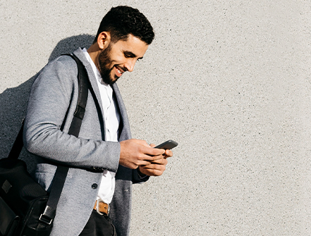 Casual young businessman using cell phone at a wall.