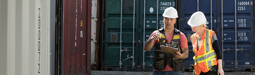 Workers inspecting empty shipping container in industrial container yard.