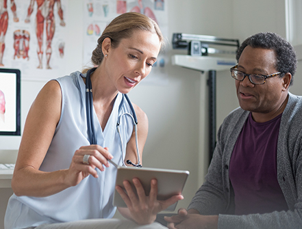 Female doctor with digital tablet talking with senior male patient in examination room.