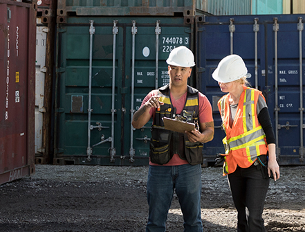 Workers inspecting empty shipping container in industrial container yard