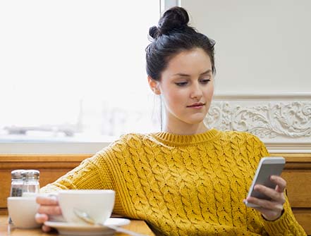 Woman texting and drinking cappuccino in cafe