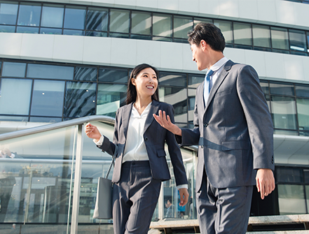 Female professional smiles at her male colleague while walking down the stairs wearing a grey suit, trying to network outside of the office. 