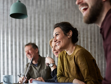 A young professional leans over a conference table with colleagues discussing treasury management services. 