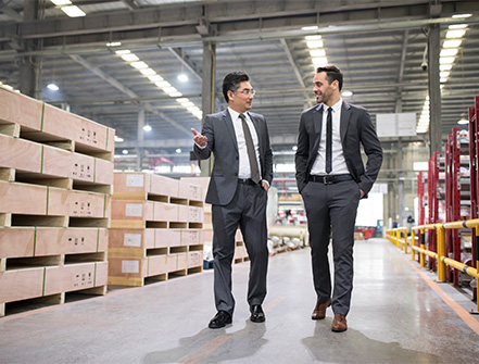 Two business men walk together through a warehouse to discuss cross-border financing.