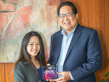 Two Cathay Bank employees in business attire pose with the Virgin Pulse award inside an office.