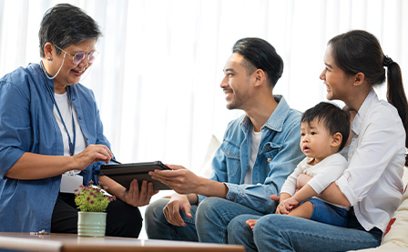 A life insurance policy manager shares a digital device with a family and their child while they sit on a couch in an office. 