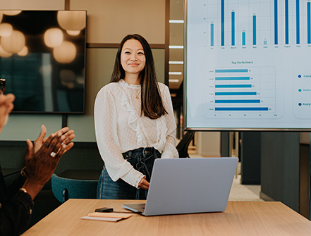 A young woman presents asset-based lending options to a meeting room full of people.