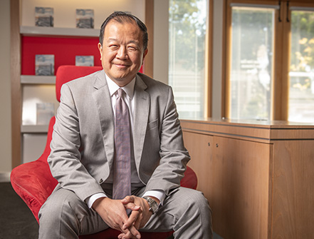 國泰銀行總裁兼首席執行官在聖馬利諾分行內拍攝專業照片，身穿棕褐色西裝，白色領襯衫，繫著玫瑰粉色領帶。