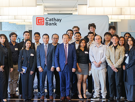 A large group of students and Cathay Bank representatives standing together in front of a Cathay Bank-branded backdrop. The group is dressed in business or business casual attire, posed for a formal group photo inside the corporate offices, with modern lighting and interior décor in the background.