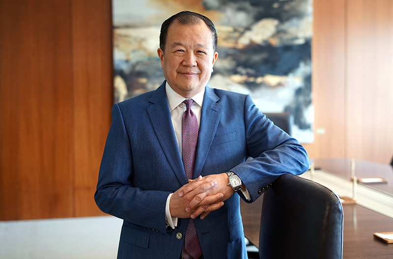 總裁兼首席執行官劉昌明先生身穿藍色西裝、繫著酒紅色領帶，站在室內一堵木鑲板牆壁和一幅抽象畫前，雙手交握，倚靠著一把會議室座椅。