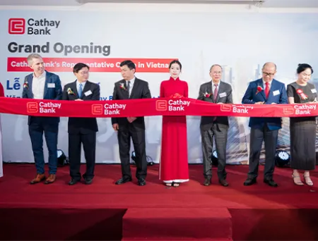 Ribbon-cutting ceremony at the grand opening of Cathay Bank's Vietnam Representative Office, with attendees holding a branded red ribbon before a Cathay Bank backdrop.