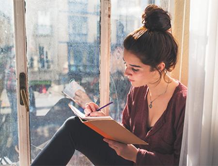 Young woman writes diary next to the window.