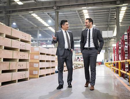 Two business men walk together through a warehouse to discuss cross-border financing.