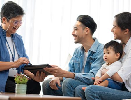 A life insurance policy manager shares a digital device with a family and their child while they sit on a couch in an office. 