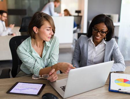 Dos mujeres de negocios conversan sobre finanzas del comercio internacional mientras miran una computadora en la oficina.