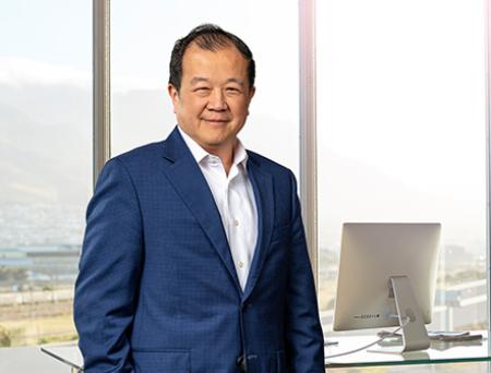 Chang M. Liu stands inside a corporate banking office wearing a dark navy suit and smiles at the camera.