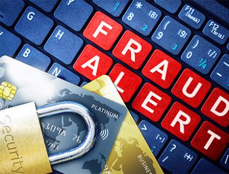 A computer keyboard displays the phrase "Fraud Alert" in red, white, and blue, with two credit cards and a security lock on top to imply awareness of scammers.