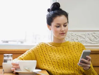 Woman texting and drinking cappuccino in cafe