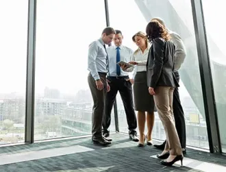 A group of office workers huddle around a digital tablet in a modern lobby.