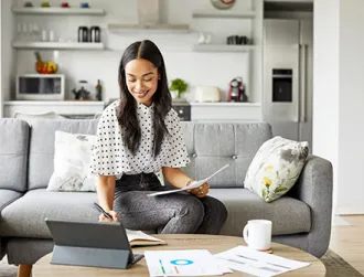 A young adult sits on her couch at home while planning for retirement on her laptop.