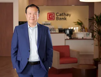 Chang M. Liu stands inside a Cathay Bank Branch wearing a dark navy suit and smiles at the camera.