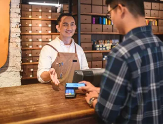 A merchant guides his client to use electronic payment method at his place of business.