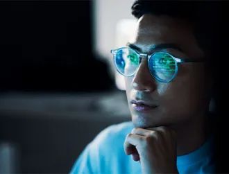 There is a close-up of a young male’s face wearing glasses, which reflects his on-screen activity from an electronic device.