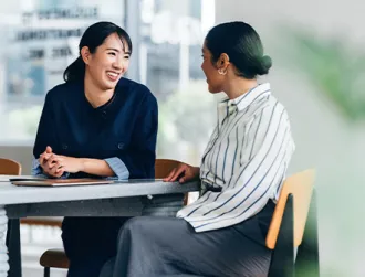 Two professional women sit at a conference table while reviewing financial literacy documents.