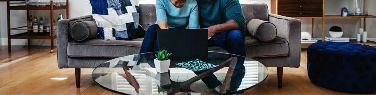 Mature married couple at home on the sofa looking at laptop