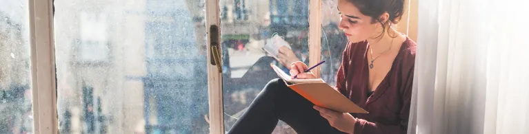 Young woman writes diary next to the window.