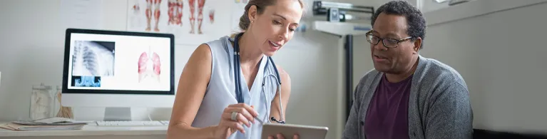 Female doctor with digital tablet talking with senior male patient in examination room.