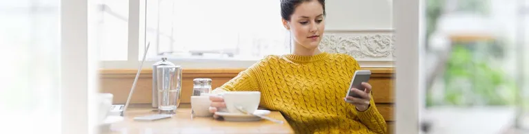 Woman texting and drinking cappuccino in cafe