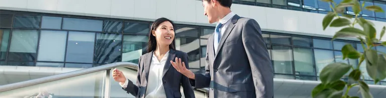 Female professional smiles at her male colleague while walking down the stairs wearing a grey suit, trying to network outside of the office. 