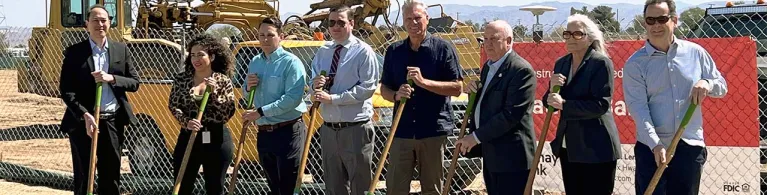 Staff from Cathay Bank and from the Federal Home Loan Bank stand on a gravel pit with shovels with other community professionals in suits.