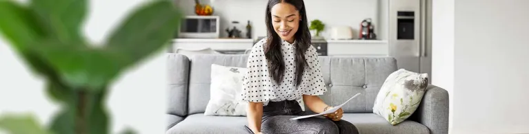 A young adult sits on her couch at home while planning for retirement on her laptop.