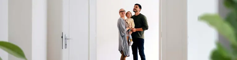 A young mom and dad hold a child in their arms while looking at a brand new home that is up for sale.
