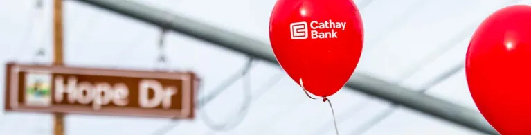 Red balloons float inside an events center with the Cathay Bank logo in white.