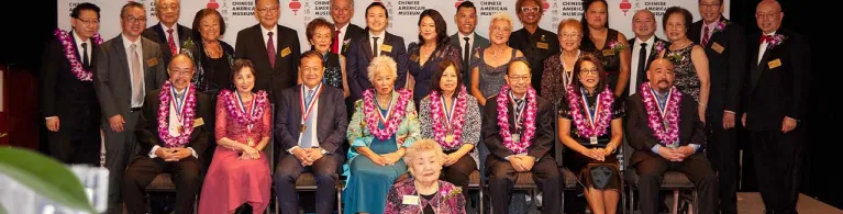 A group of people sit on the front row and stand on the back row on a stage as special guests and honorees for the Chinese American Museum’s Historymakers Gala in Los Angeles.