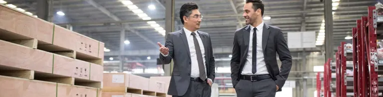 Two business men walk together through a warehouse to discuss cross-border financing.