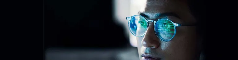 There is a close-up of a young male’s face wearing glasses, which reflects his on-screen activity from an electronic device.