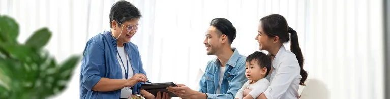 A life insurance policy manager shares a digital device with a family and their child while they sit on a couch in an office. 
