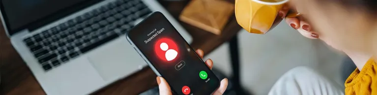 Over the shoulder view of young Asian woman receiving an incoming suspected call from unknown caller on her smartphone and rejecting the call at home. Device screen showing warning sign as detected by the network provider.