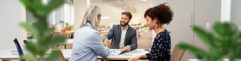Business professional meeting with clients, shaking hands over documents during a discussion on analyzed business checking solutions.